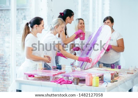 Four female students with teacher finishing painting circle canvas picture together with pouring acrilic method creating fluid acrylic abstract in art therapy class. Art, design, creating concept. Royalty-Free Stock Photo #1482127058