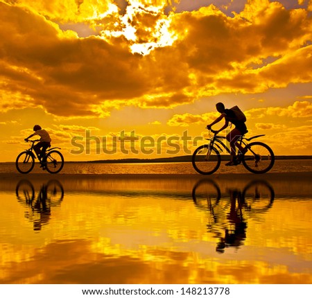 silhouettes of mother and child on bicycle against sunset sky With reflection on water Copy space for inscription 