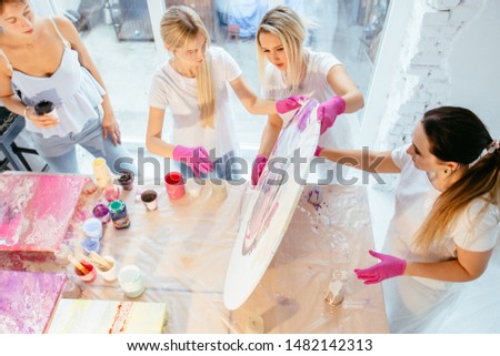 Four female student painting circle canvas picture with pouring acrilic method creating fluid acrylic abstract in art therapy class. Art, design, creating concept. View from above Royalty-Free Stock Photo #1482142313