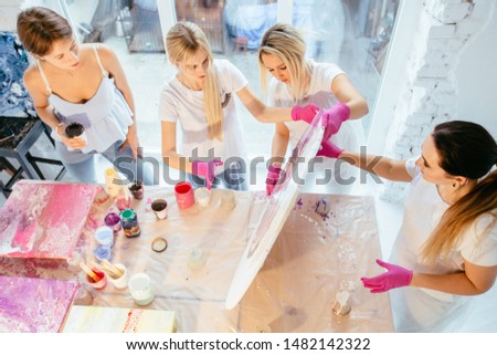 Four female student painting circle canvas picture with pouring acrilic method creating fluid acrylic abstract in art therapy class. Art, design, creating concept. View from above Royalty-Free Stock Photo #1482142322