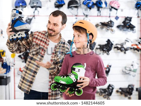 positive english male shop assistant helping boy to choose roller-skates in sports store
