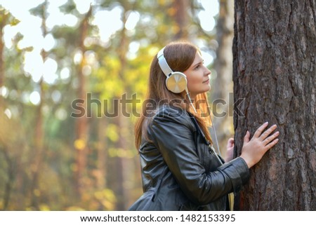 Woman and autumn. Red-haired girl in white headphones looking at the tree. Earphones connected to the tree