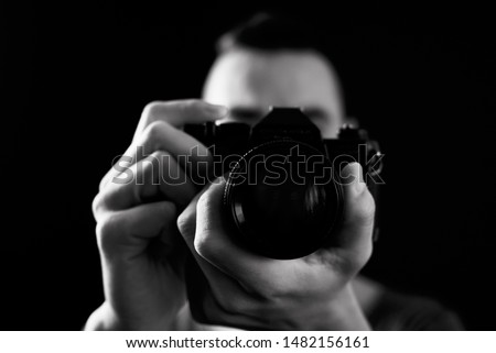 closeup of a young man looking through the viewfinder of a reflex camera, pointing to the observer, about to press the shutter button, in black and white