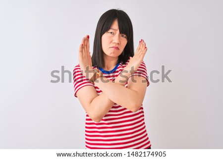 Young beautiful chinese woman wearing red striped t-shirt over isolated white background Rejection expression crossing arms doing negative sign, angry face