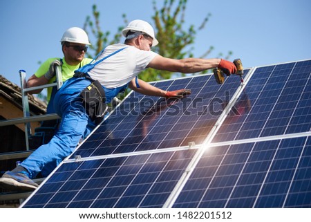 Two workers technicians installing heavy solar photo voltaic panels to high steel platform. Exterior solar system installation, alternative renewable green energy generation concept. Royalty-Free Stock Photo #1482201512