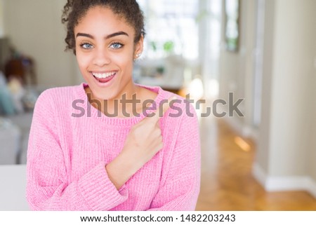 Beautiful young african american woman with afro hair cheerful with a smile of face pointing with hand and finger up to the side with happy and natural expression on face