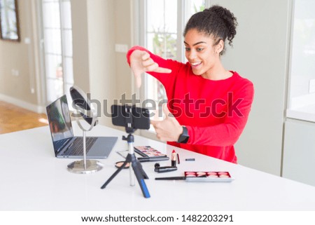 Young african american influencer woman recording make up tutorial smiling making frame with hands and fingers with happy face. Creativity and photography concept.
