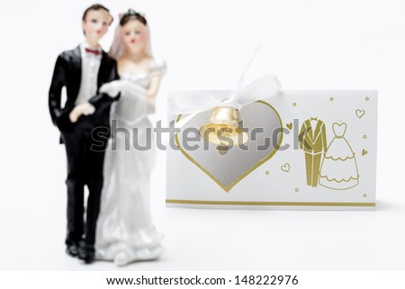 miniature statue of a bridal couple in front of wedding invitation, decorated with a bell 