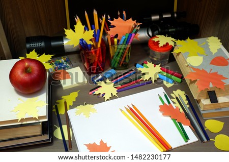 Back to school concept with empty sketchbook, colored pencils, stationary supplies and schoolbooks on brown wooden table with apple and decorative autumn leaves