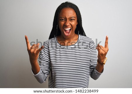 Young african american woman wearing striped t-shirt standing over isolated white background shouting with crazy expression doing rock symbol with hands up. Music star. Heavy concept.