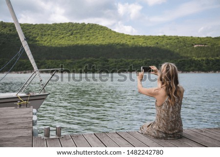 girl blogger traveler sits on a pier and takes pictures on a smartphone beautiful mountain lake and yachts