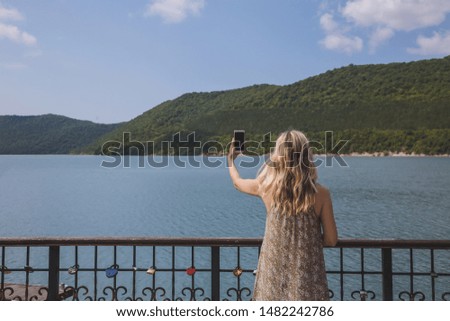 girl blogger traveler takes pictures on smartphone beautiful mountain lake and yachts