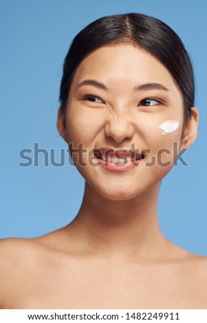 An Asian-looking woman with bare shoulders and a white cream on her face smiles at the camera