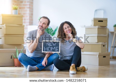 Middle age senior couple sitting on the floor holding blackboard moving to a new home serious face thinking about question, very confused idea