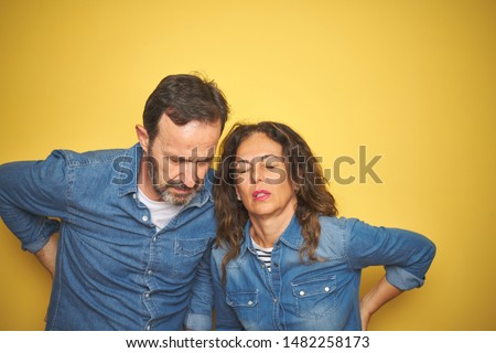 Beautiful middle age couple together standing over isolated yellow background Suffering of backache, touching back with hand, muscular pain