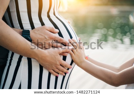 Picture of man and children hugging pregnant woman's belly on summer day