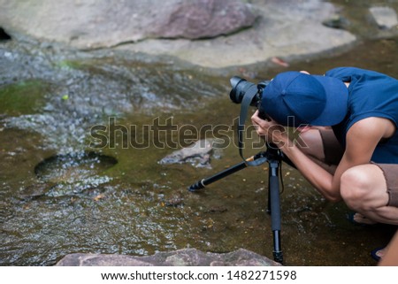 People are using camera to take pictures of waterfall in forest.