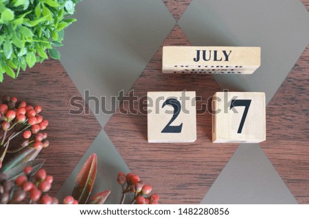 July 27. Date of July month. Number Cube with a flower and leaves on Diamond wood table for the background