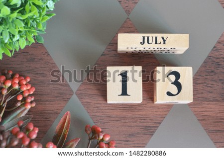 July 13. Date of July month. Number Cube with a flower and leaves on Diamond wood table for the background