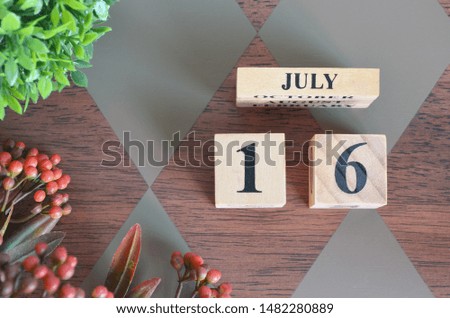 July 16. Date of July month. Number Cube with a flower and leaves on Diamond wood table for the background
