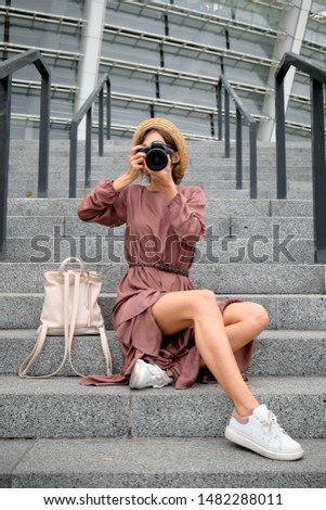 Beautiful girl photographer sits on the steps and takes pictures outdoors