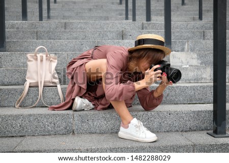Woman photographer in a hat sits on the steps and takes pictures outdoors