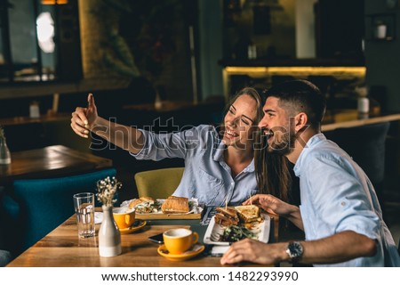 happy young couple taking picture while eating in cafeteria