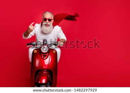 Portrait of funky pensioner in eyewear eyeglasses showing rock-and-roll sign driving bike wearing white jumper isolated over red background