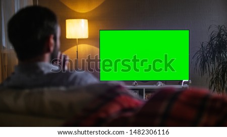 In the Evening Back View of a Middle Aged Man Sitting on a Couch Watching Big Flat Screen TV.