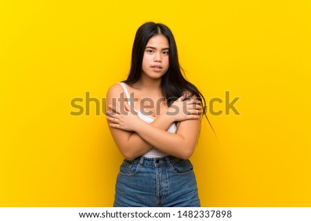 Young teenager Asian girl over isolated yellow background freezing