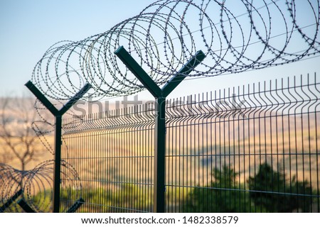 Steel grating fence of soccer field,Metal fence wire with bokeh in the background . Coiled razor wire with its sharp steel barbs on top of a wire mesh perimeter fence ensuring safety and security.