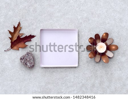 Composition with empty square metal tray, candlelight and maple leaves.