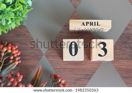 April 3. Date of April month. Number Cube with a flower and leaves on Diamond wood table for the background