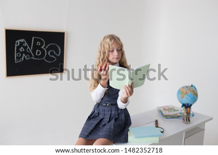 Blond girl at the blackboard with book and apple. Back to school.