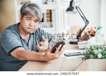 Blurred of Asian man, He is patient from neurological diseases, or hemiplegia having a facial palsy and kinking fingers, He is looking at the alarm clock in his hand, to health paralysis concept. Royalty-Free Stock Photo #1482357047