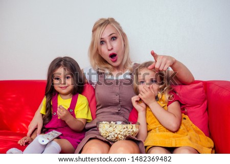 Portrait of happy two daughter and mother watching cartoons with popcorn on a red couch