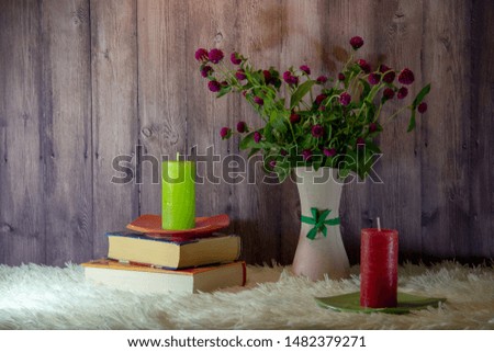 A bouquet of wildflowers in a vase, books, two candles on saucers on a fluffy white bedspread, wooden background.