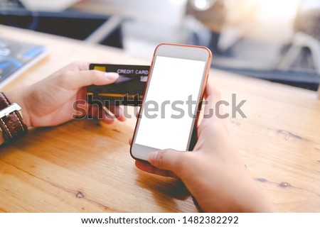 Close up of woman using blank cell phone and credit card sending massages shopping online or reporting lost card, fraudulent transaction in the coffee shop.