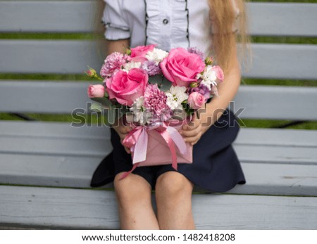 School girl dressed in school uniform holding a bright pink festive bouquet of beautiful flowers for teacher. No face. Blurred background.