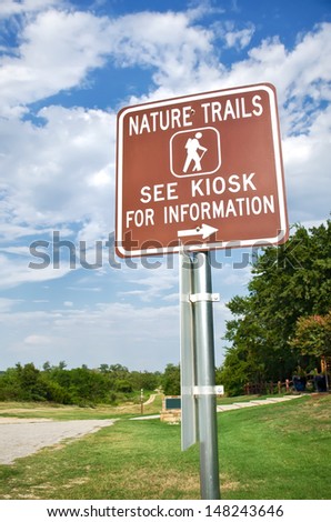 Nature trail sign for information in a park on a sunny summer day. Trees and blue sky with clouds on background.   
