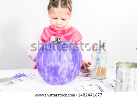Little girl painting small craft pumpkin with purple acrylic paint.