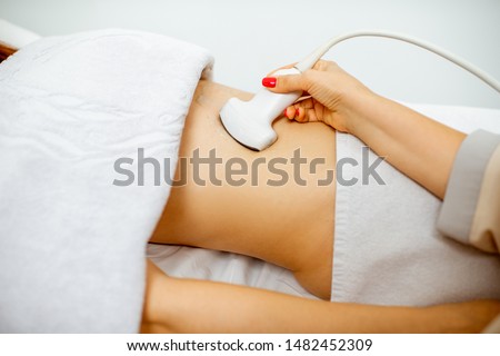 Doctor performs ultrasound examination of a women's pelvic organs or diagnosing early pregnancy at the medical office. Close-up view with no face Royalty-Free Stock Photo #1482452309