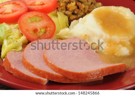 Sliced ham dinner with salad, cornbread stuffing, mashed potatoes, and country gravy - shallow depth of field, focus on ham