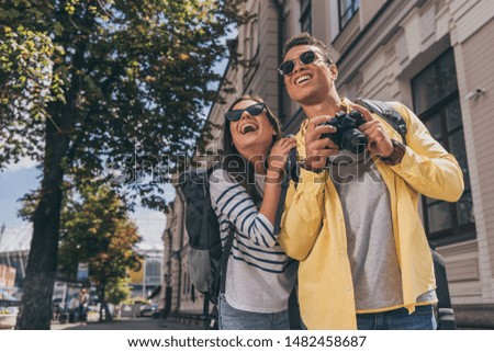 Woman and bi-racial friend with backpacks smiling and taking pictures
