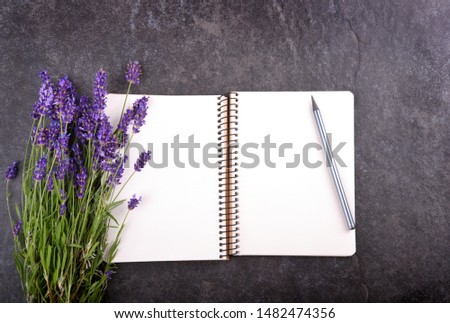 Top view of open blank notepad with lavender bouquet on black stone background, copy space for your text