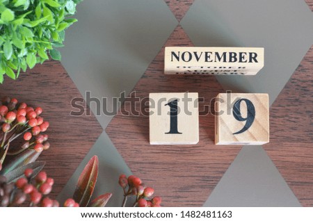 November 19. Date of November month. Number Cube with a flower and leaves on Diamond wood table for the background