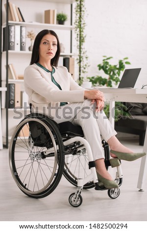 confident disabled businesswoman looking at camera while sitting in wheelchair in office