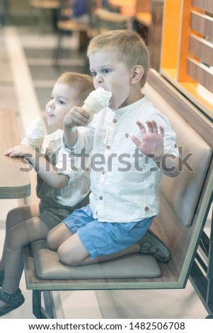 Two little boy eating and licking ice cream in a cafe/ Selective focus/ Taking a picture through a shop window