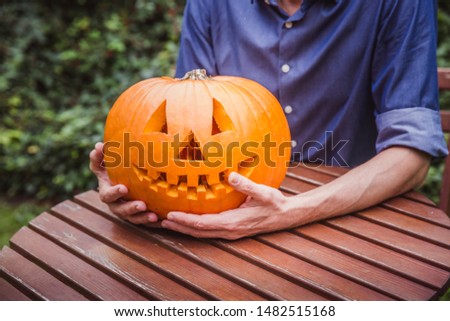 Man in blue shirt holding big pumpkin in front of his face. Happy Halloween