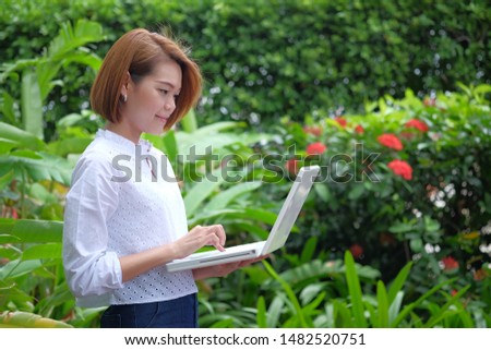 Portrait of a woman standing holding a laptop pc. Smiling woman at green outdoor with copy space